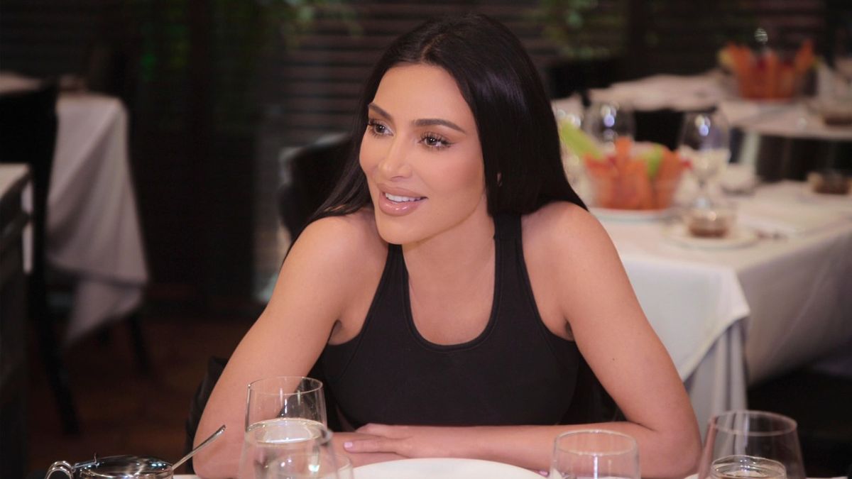 Kim Kardashian leaning her arms on a table and smiling.