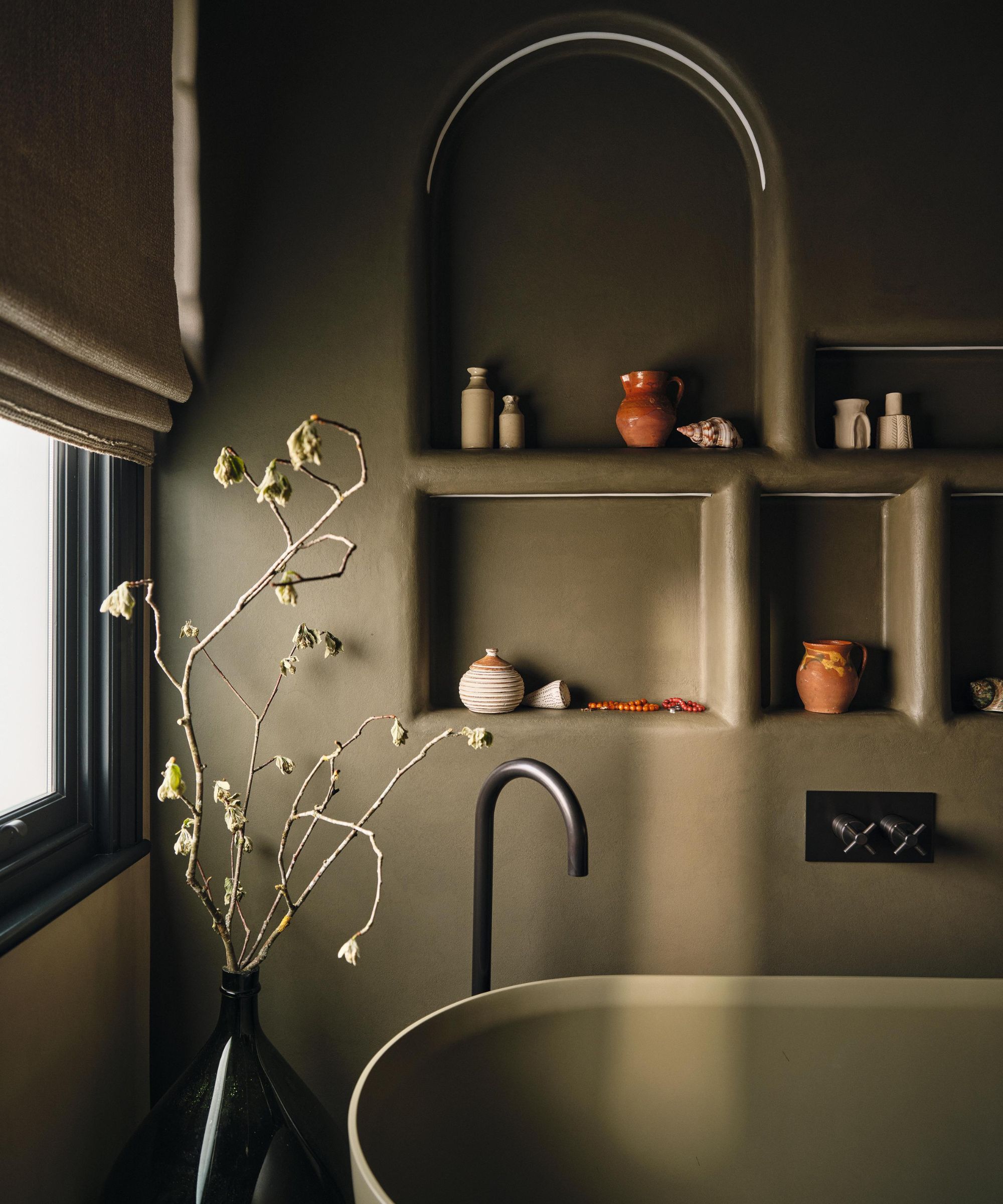 a dark green moody bathroom with color drenched tub and arched niche shelving