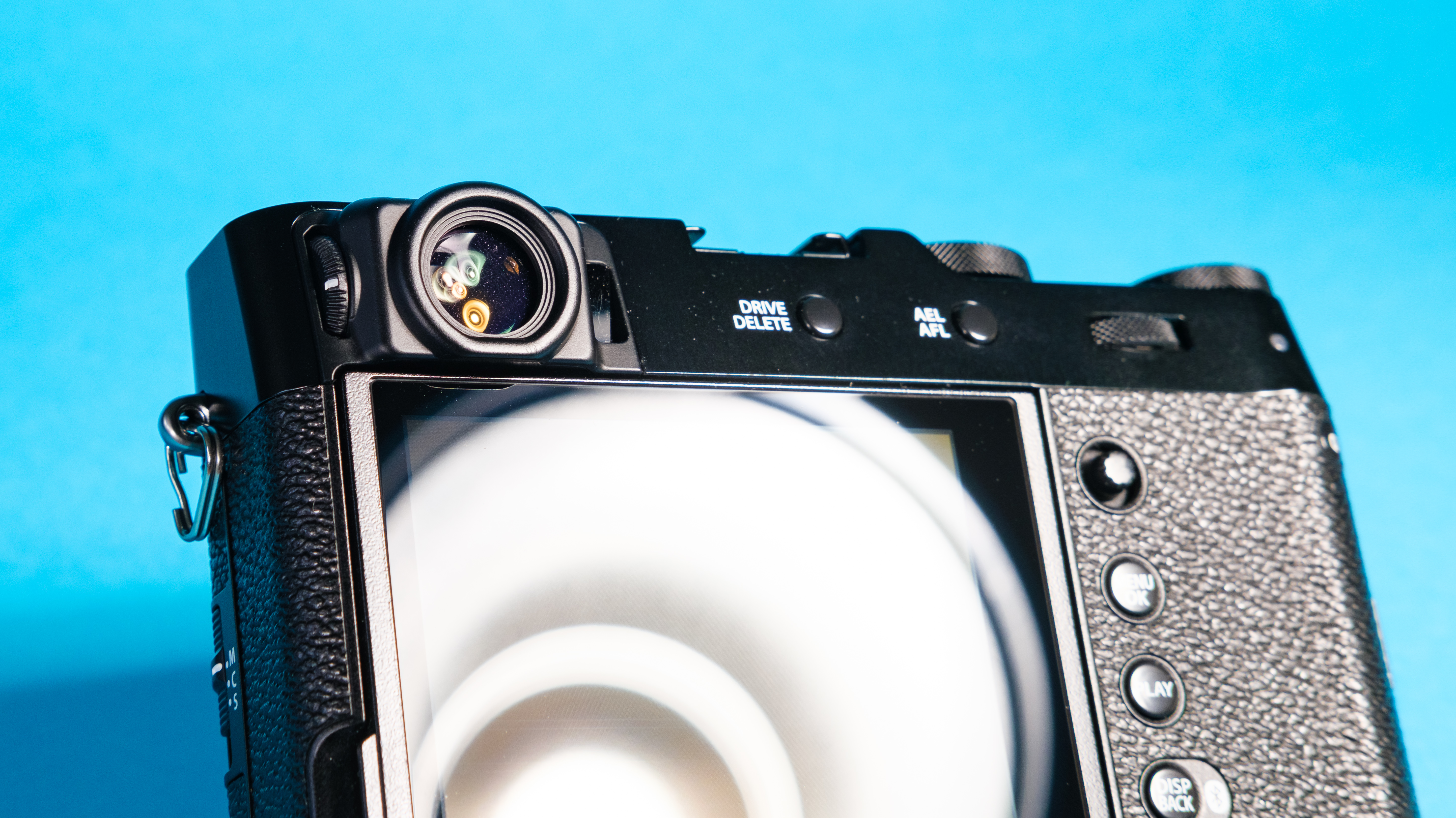 The rear of the Fujifilm X100VI mirrorless camera against a blue background with the viewfinder window showing.