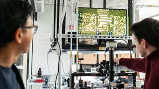 Two people in a lab using a microscope to view the chip on a monitor.