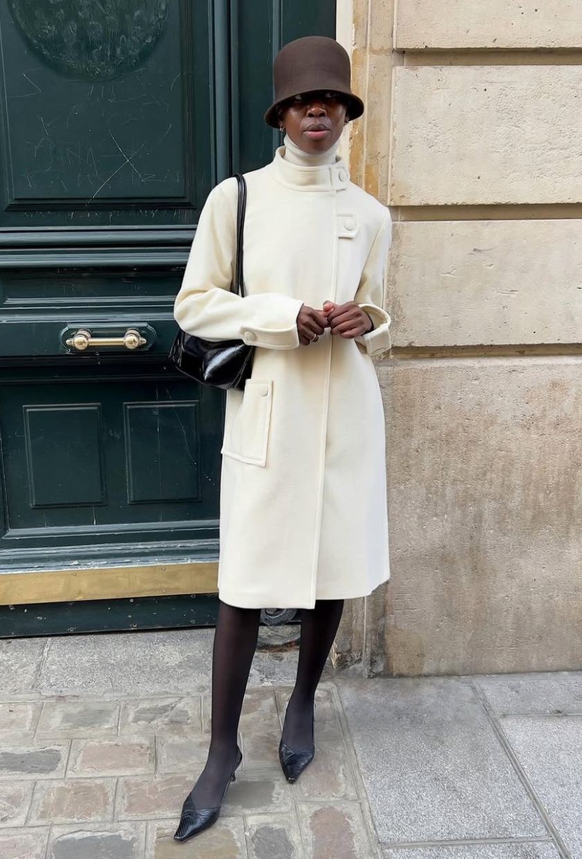 @sylviemus_ wears white wool coat, brown bucket hat, black tights and black mules