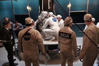 Mercury astronaut Alan Shepard (in spacesuit), portrayed by Jake McDorman, climbs into his Mercury capsule with help from Mercury astronaut John Glenn (with NASA logo, center), played by Patrick J. Adams, in the season finale of the National Geographic series "The Right Stuff," now streaming on Disney+.