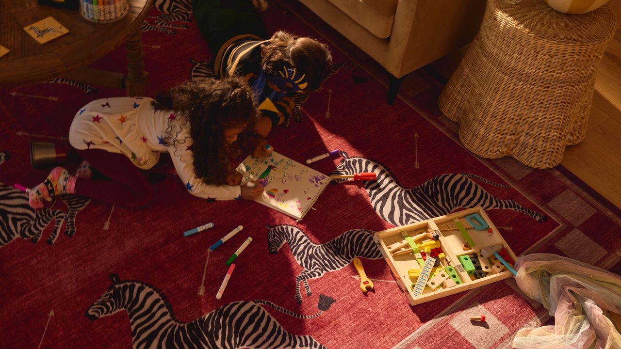 Ruggable x Scalamandr&eacute; animal print zebra rug on the floor of a living room with kids coloring on it