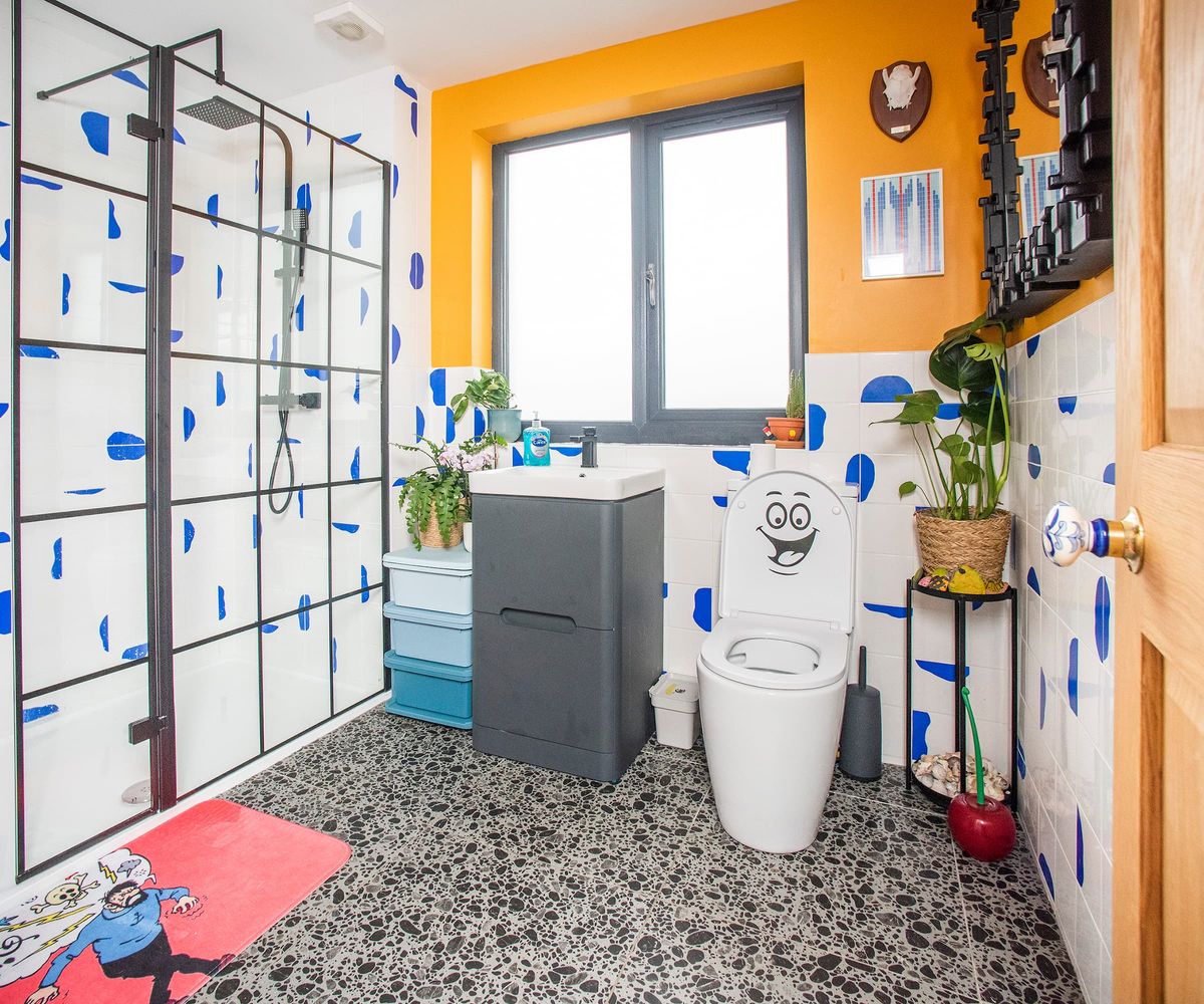 A bathroom with a walk-in shower and blue shaped blots on the white tiled walls