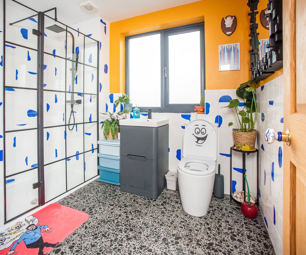 A bathroom with a walk-in shower and blue shaped blots on the white tiled walls