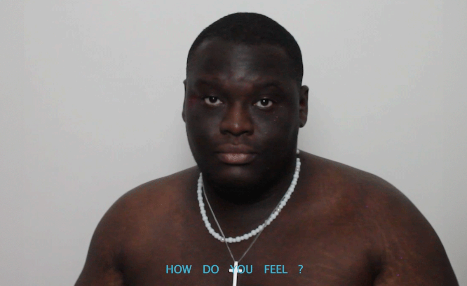 man's face, wearing only a necklace, looking at camera