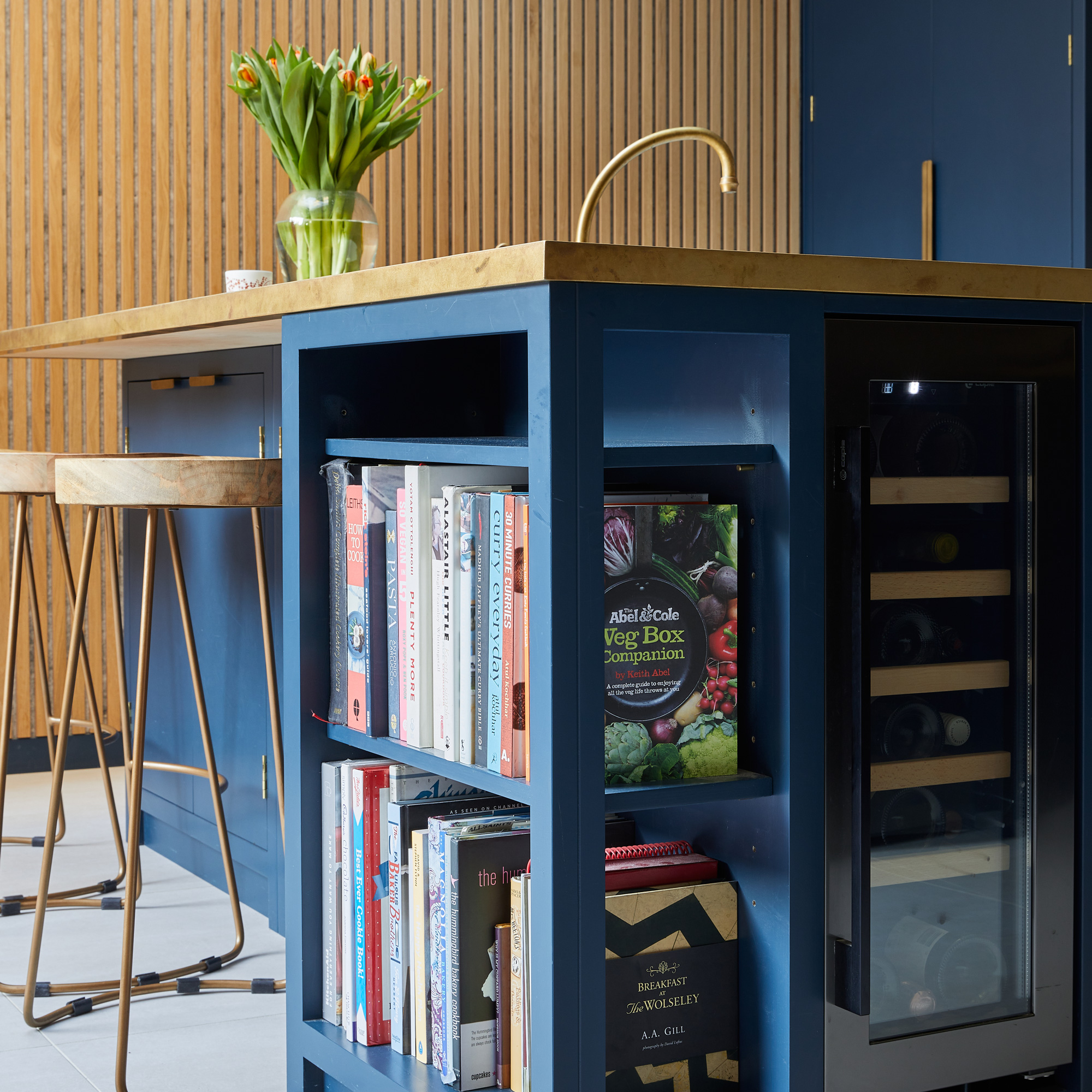 a dark blue kitchen island with corner shelving space filled with cookbooks and a small wine fridge