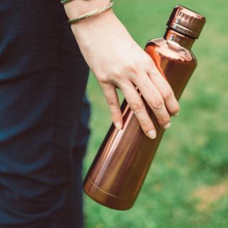 A person holding a rose gold water bottle.