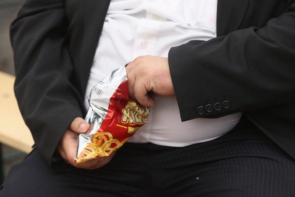 An obese man eats chips.