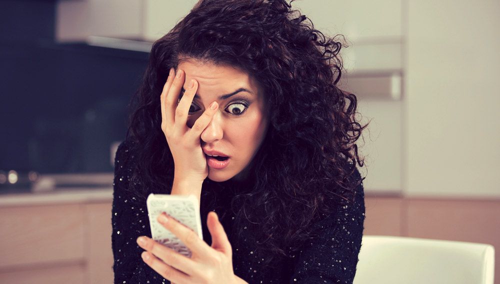 Young woman reacting in fright to something she sees on her smartphone.