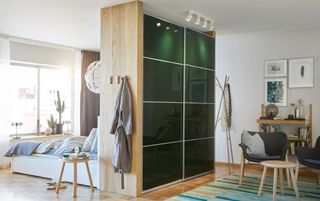 A bedroom divided into a dressing room with a Pax wardrobe with green Hokksund sliding doors