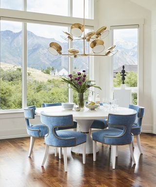 A kitchen diner with a breakfast area in a bay window, with views of mountains, white round table and turquoise blue modern chairs