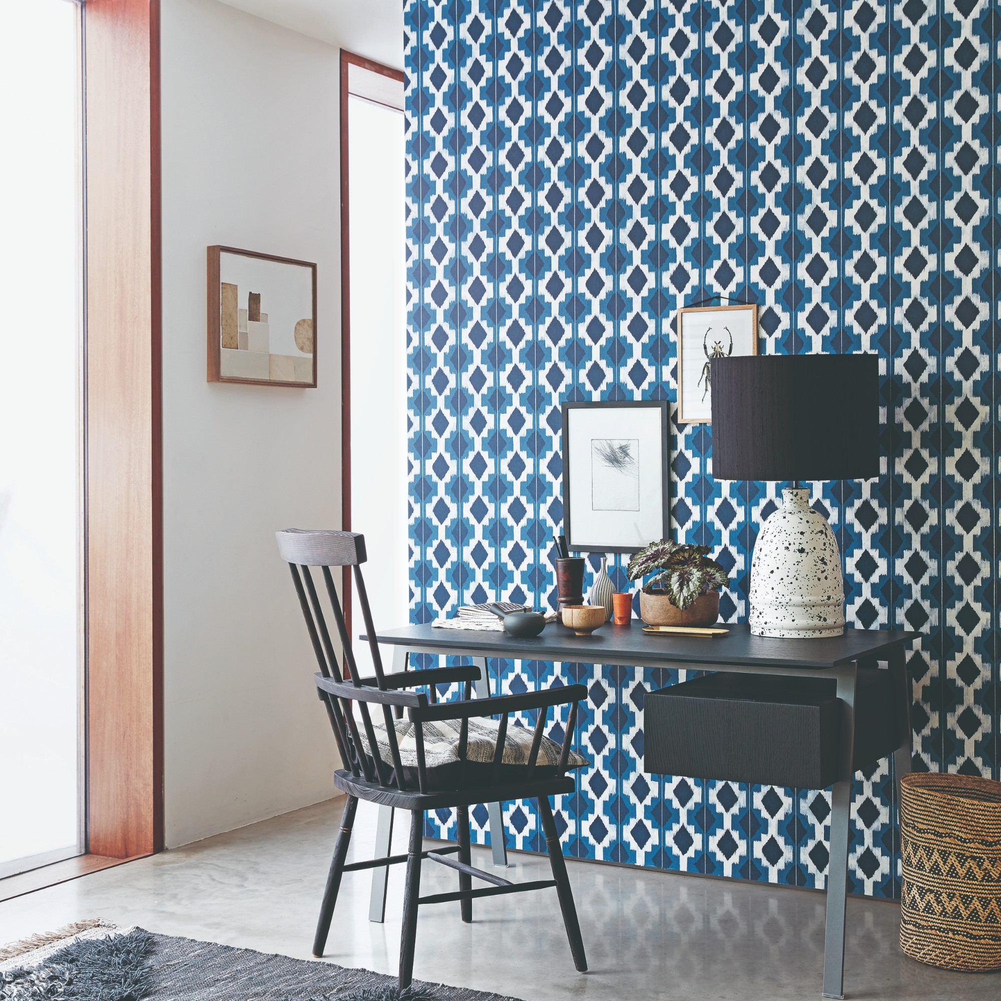 A home office area in a bedroom with a wall coevered in a blue geometric wallpaper