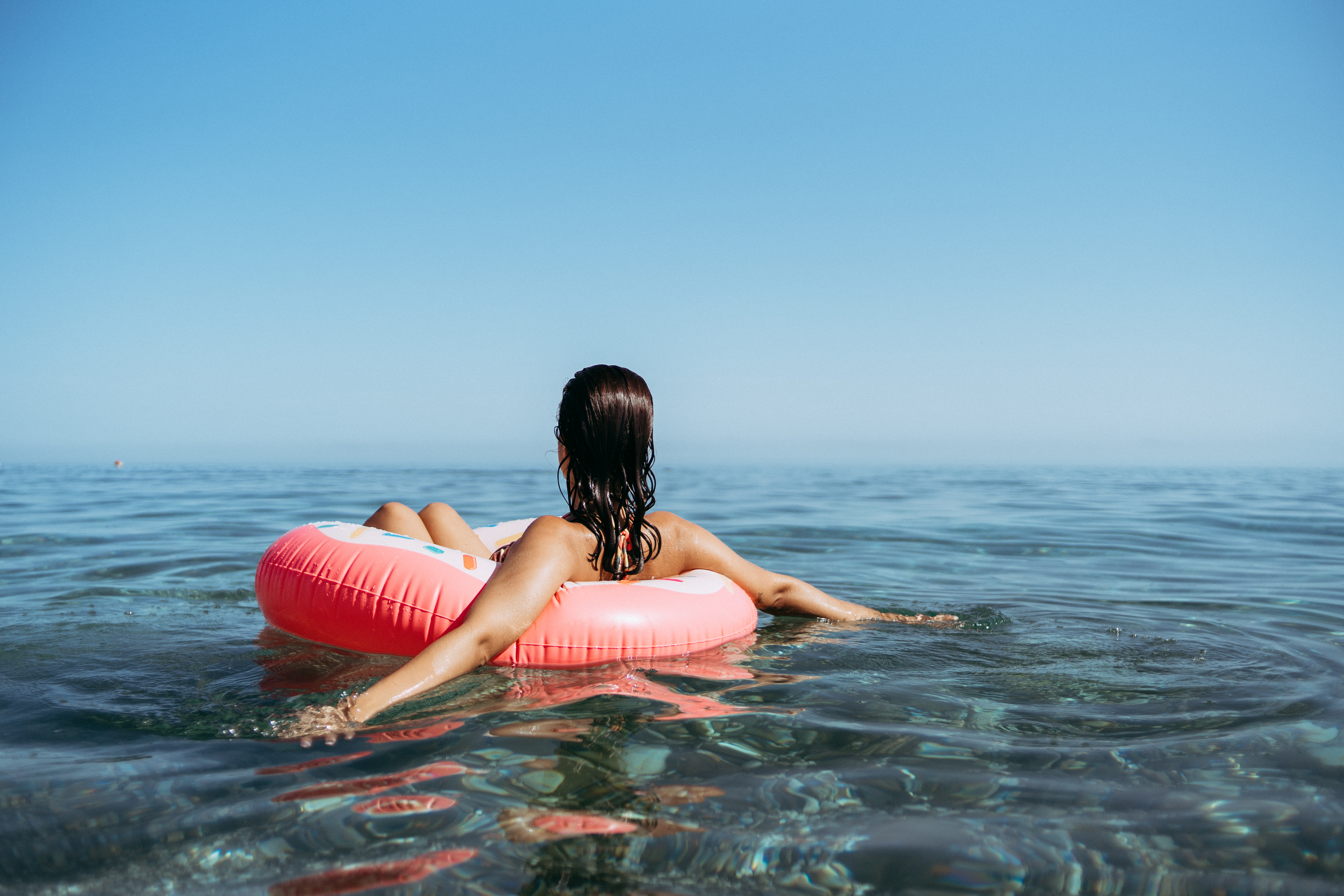 a woman floating in the ocean on a pink inner tube facing away from the camera