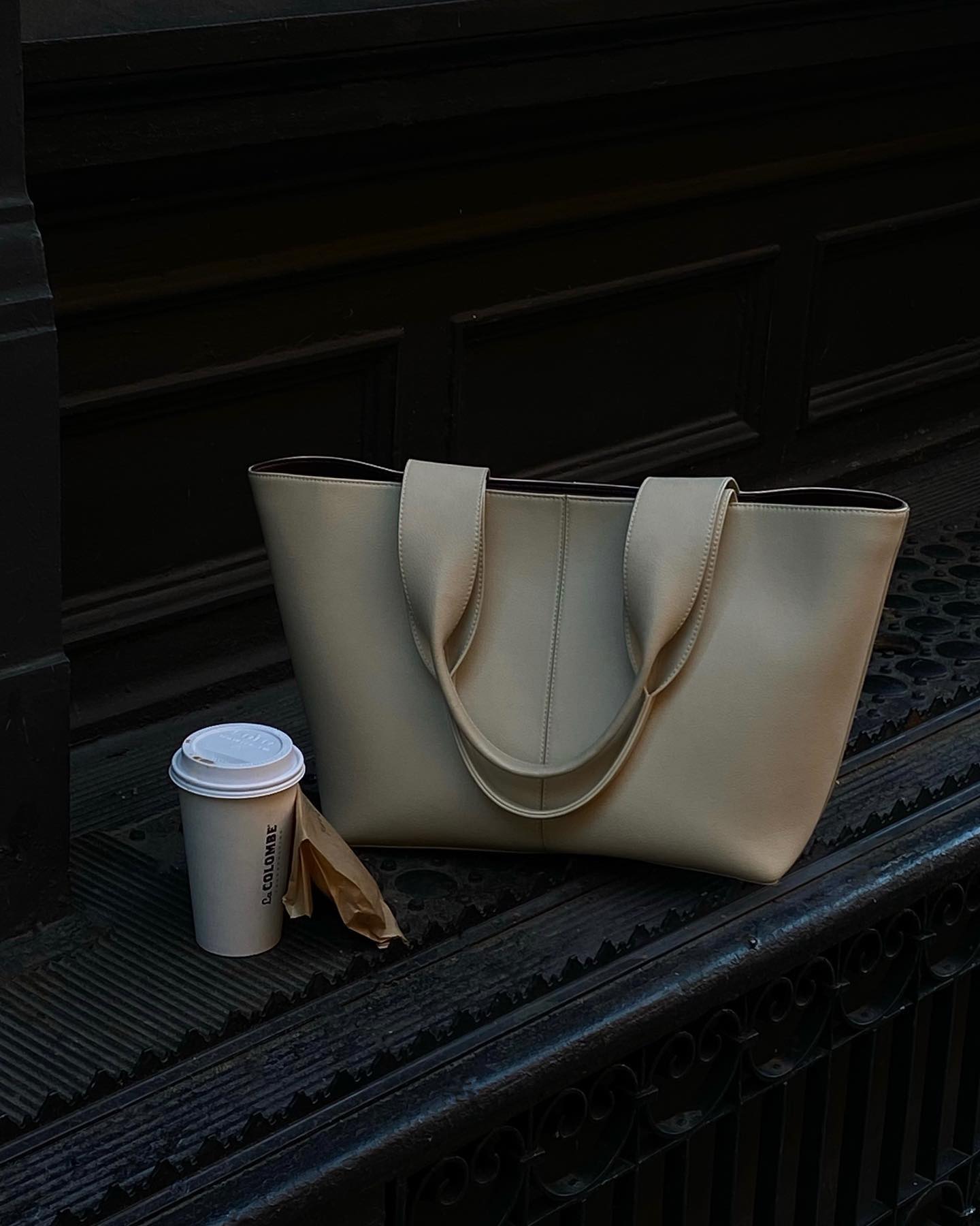Off-white Freja NYC oversize tote bag with coffee cup sitting on dark brown park bench.