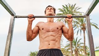 Calisthenics: Man performing a pull-up outside in the park using a bar
