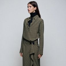 A close-up shot of a model wearing a black turtleneck top and green check midi dress with a belt from Zara