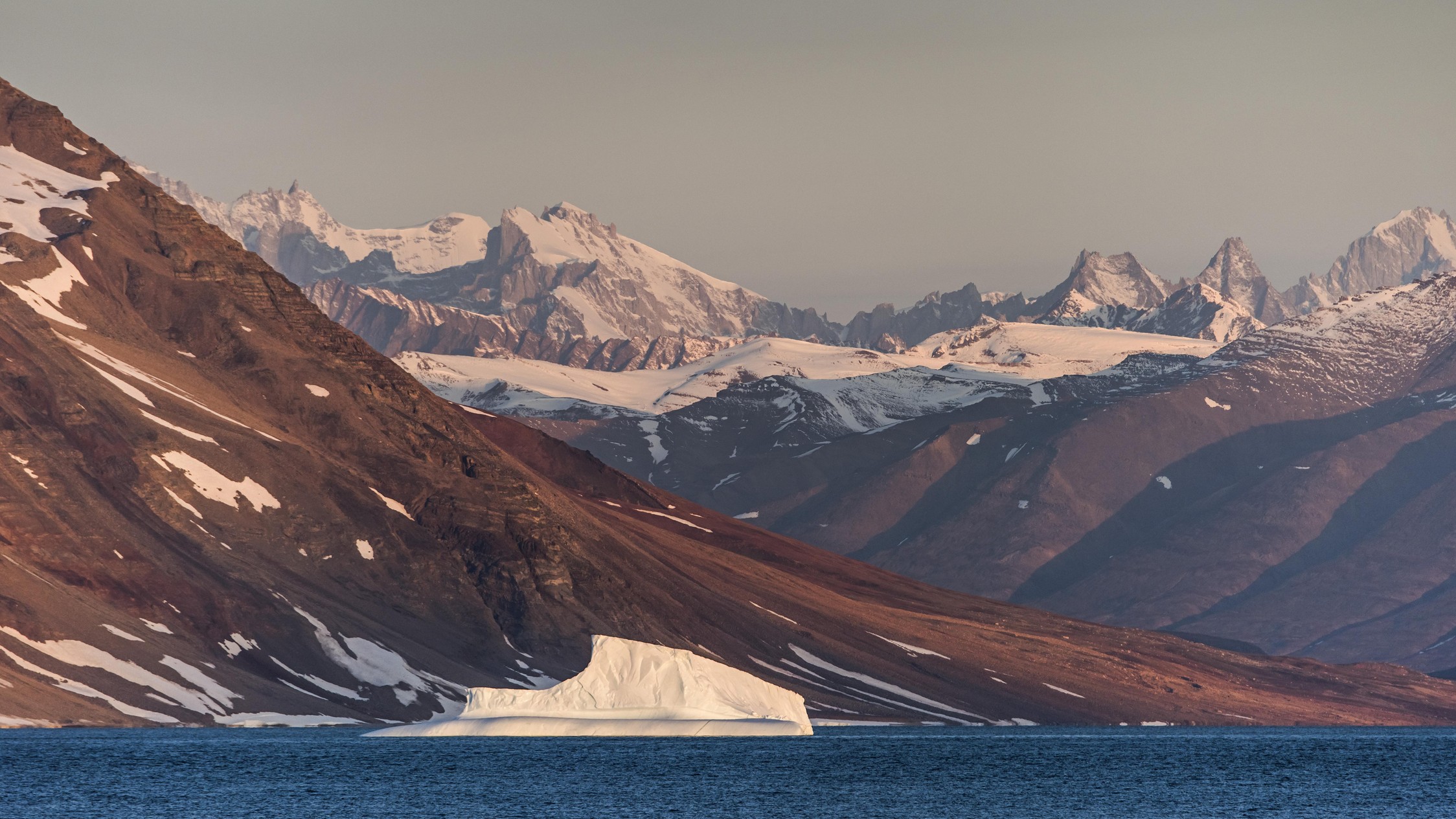 serene fjord in a golden hue with snow-capped mountains and deep blue water below.