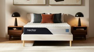 The new Nectar Classic Mattress shown on a white bedframe, dressed with orange, and black and white pillows