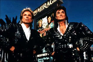 Siegfried and Roy standing on the Las Vegas strip with a sign for The Mirage behind them