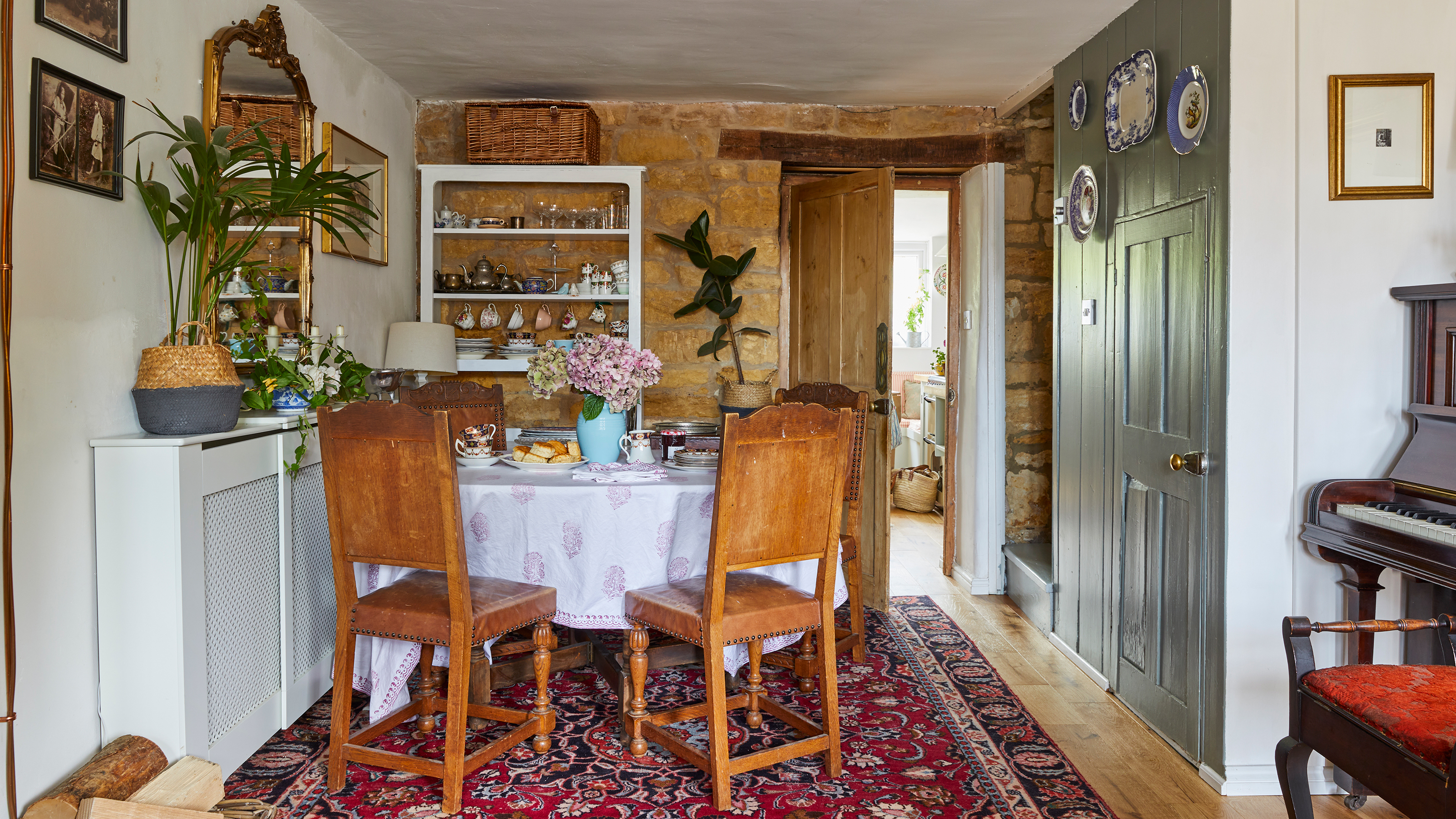 Dining area in a small period cottage with exposed stone wall behind and door through to kitchen