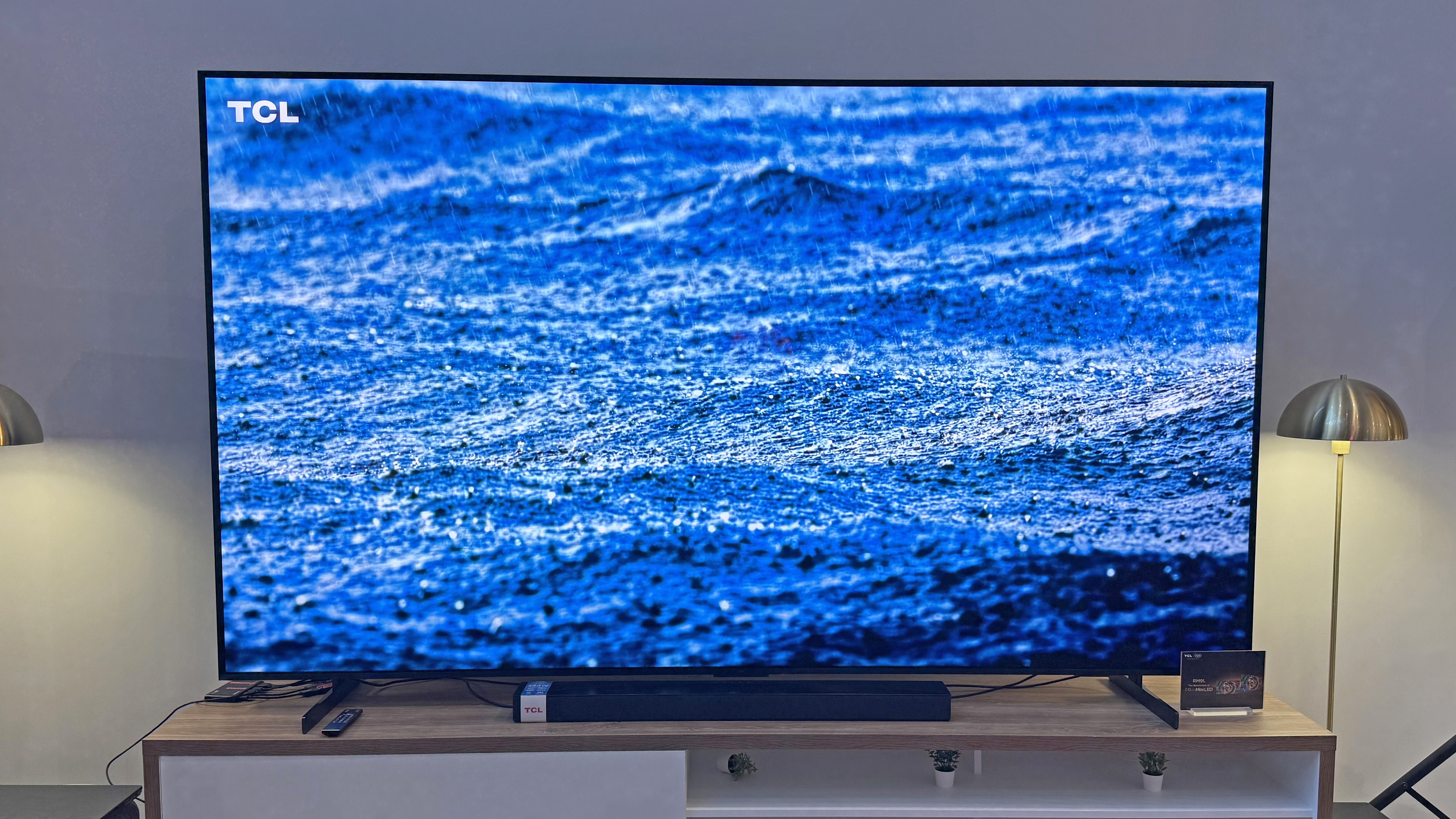 The TCL RM9L TV at a launch event, showing an image of rain falling on the ocean, with a striking blue tone and lots of detail in the rain splashes