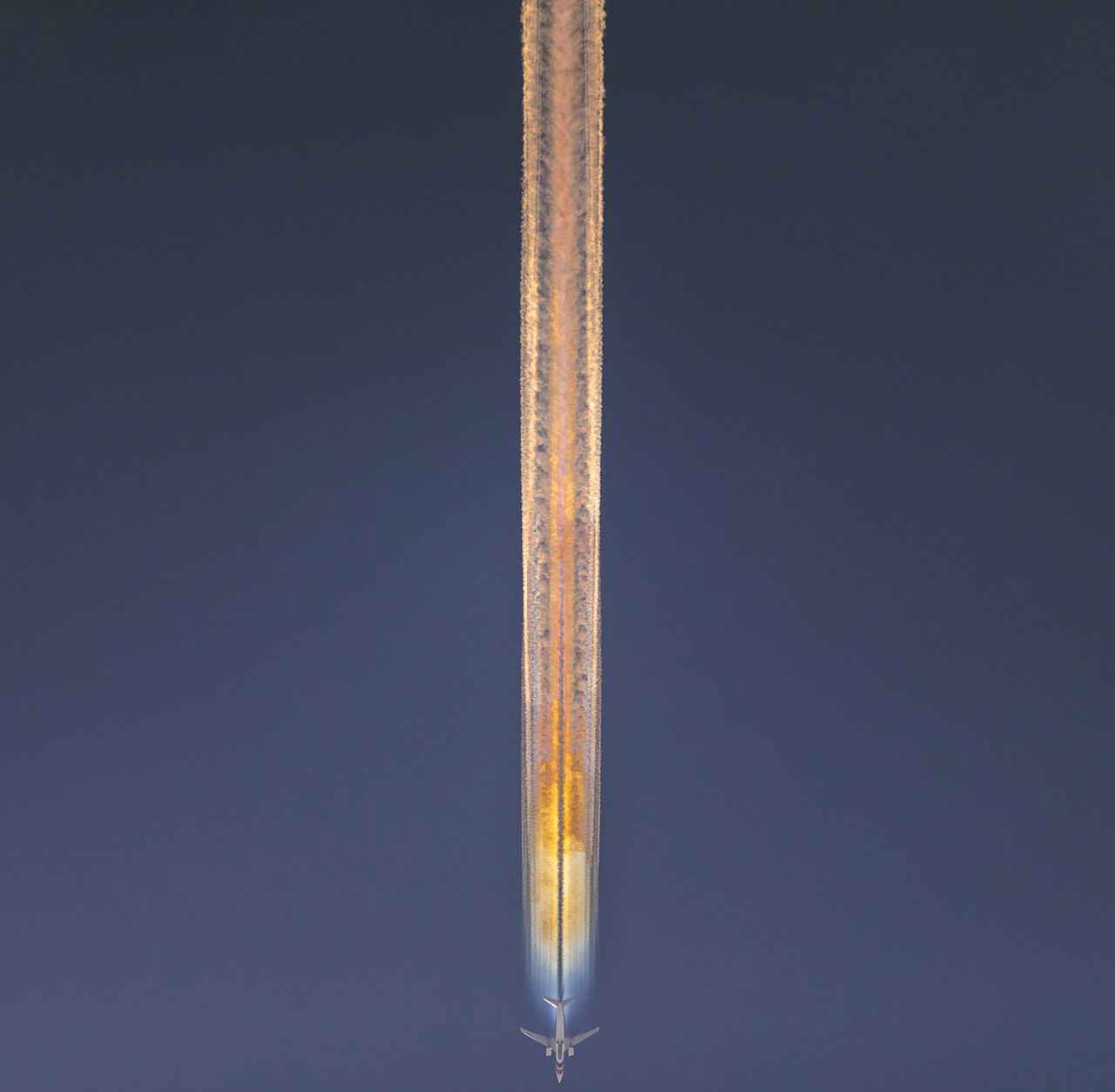 rainbow contrails behind an airplane in front of a blue sky.