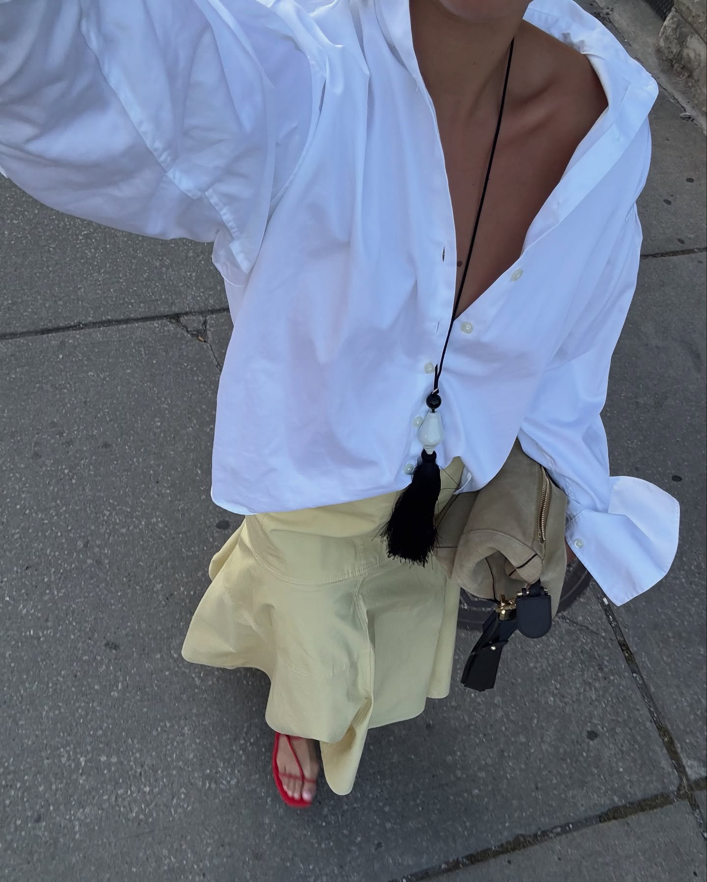 Sasha Mei wears an oversized white shirt, yellow maxi skirt and red sandals.