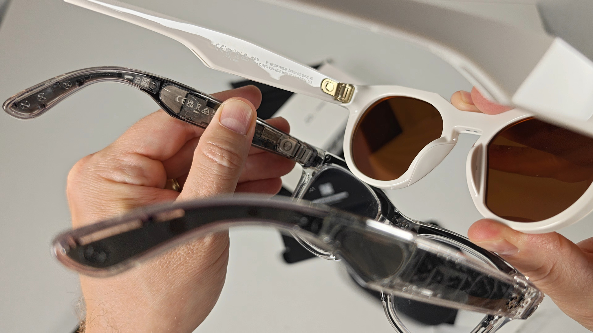 Comparing the power sliders on the inside of the left arm of a transparent pair of Ray-Ban Meta Smart Glasses with Oakley Meta Smart Glasses
