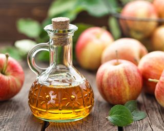 Bottle of apple cider vinegar next to apples on a wooden table