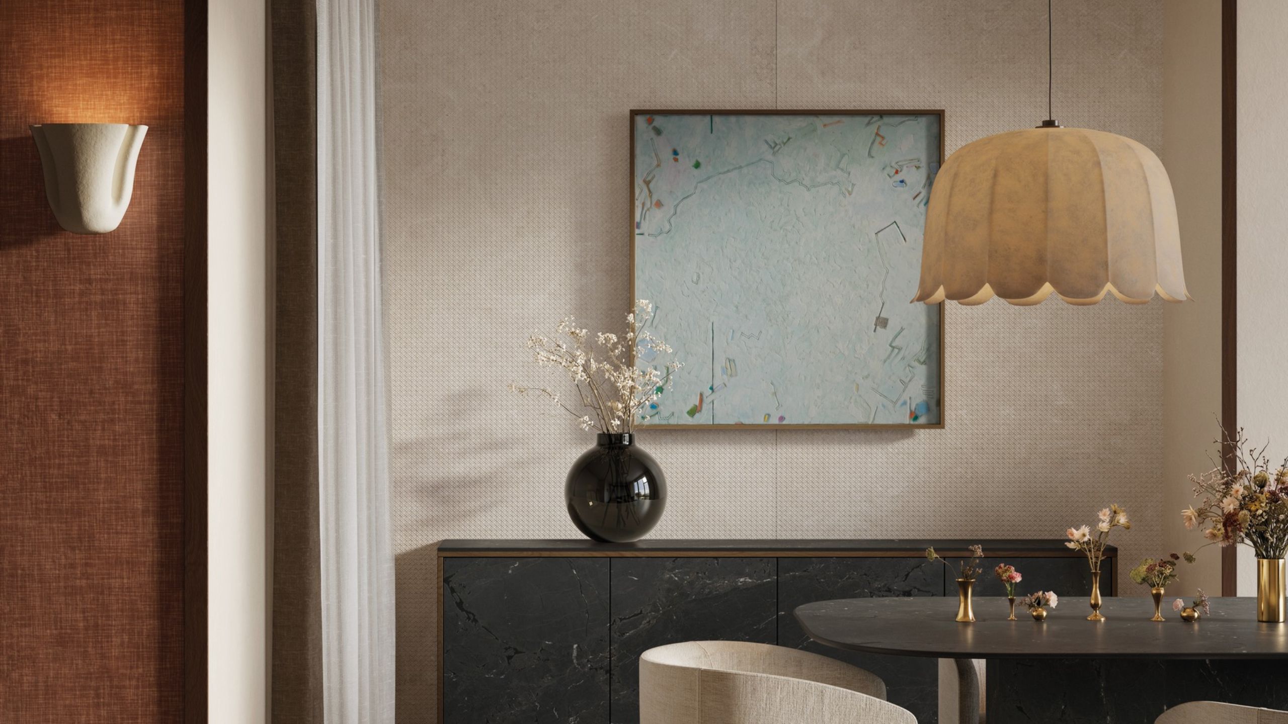 A neutrally tinted interior with a floral-inspired pendant lamp in paper, an abstract pale blue artwork, a round glossy vase filled with flowers, textile-clad brown walls, and a white ceramic sconce.