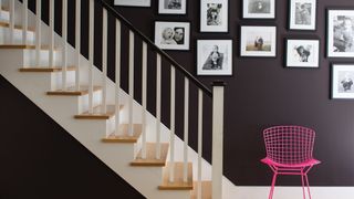 deep burgundy wall behind white painted staircase spindles and a gallery wall above, bight pink neon chair