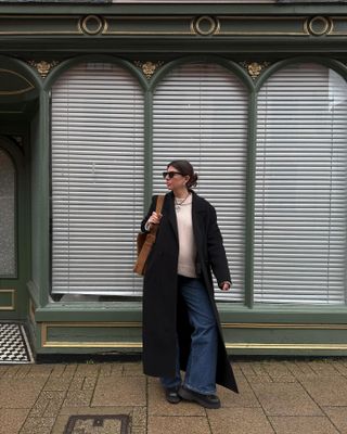 Influencer wearing black coat, white sweater, jeans, black boots, and brown suede tote bag.