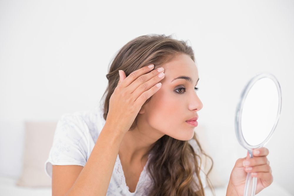 A woman looks at her skin in the mirror closely 