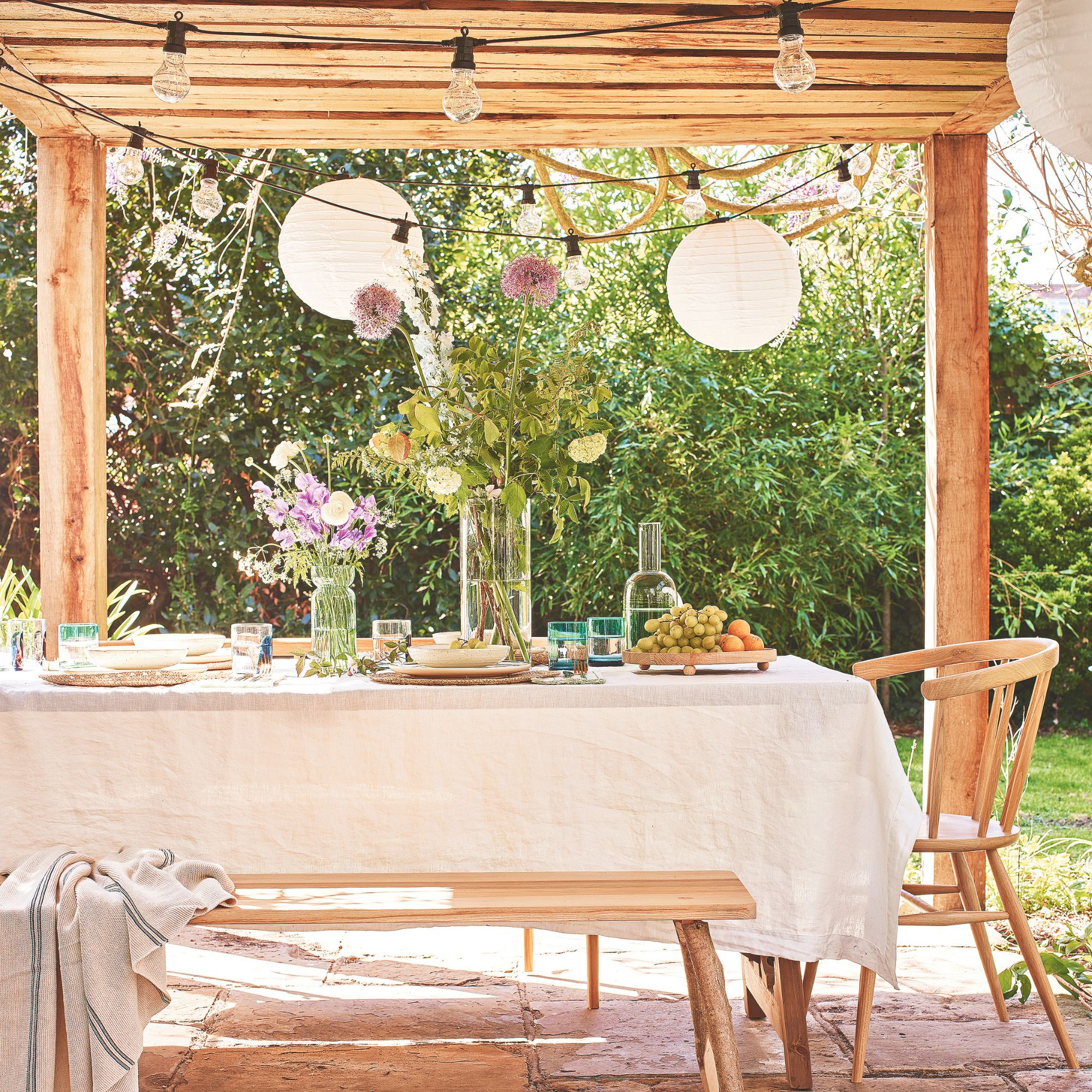 Outdoor dining area underneath a pergola, with a dining table filled with food and flowers