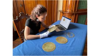a woman sitting at a table examines a disk-shaped bronze astronomical instrument.