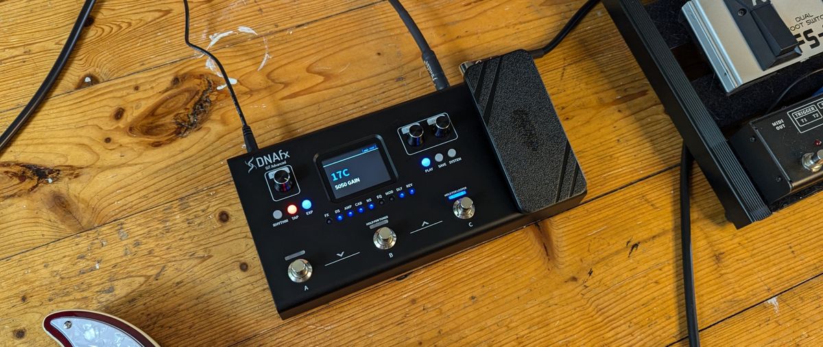 A Harley Benton DNAfx GiT Advanced multi-effects pedal lying on a wooden floor with an electric guitar