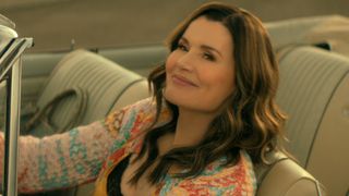 Geena Davis driving a car and looking up and smiling. 