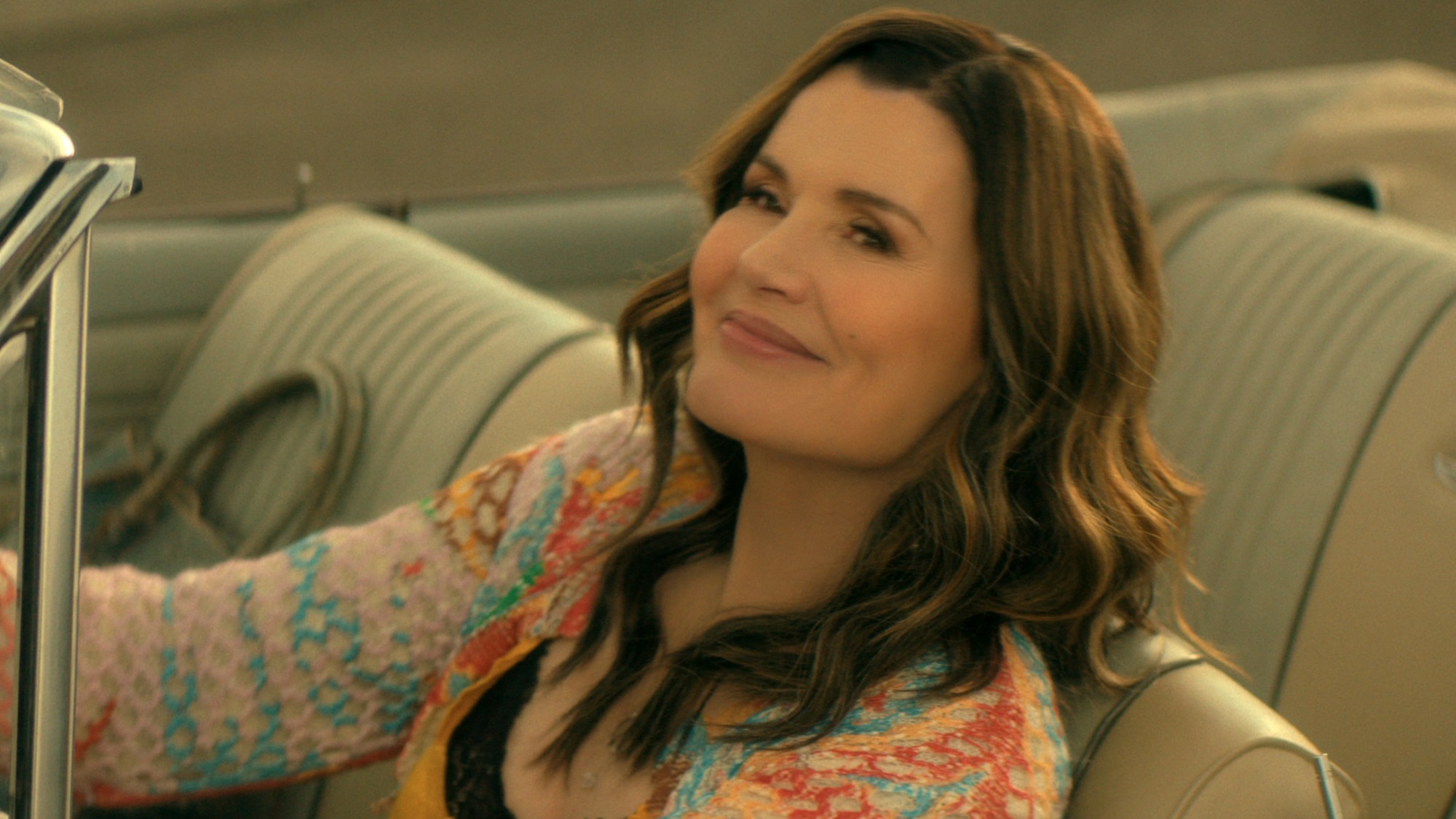 Geena Davis driving a car and looking up and smiling. 