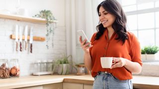 A lady looks on her phone while drinking a cup of coffee