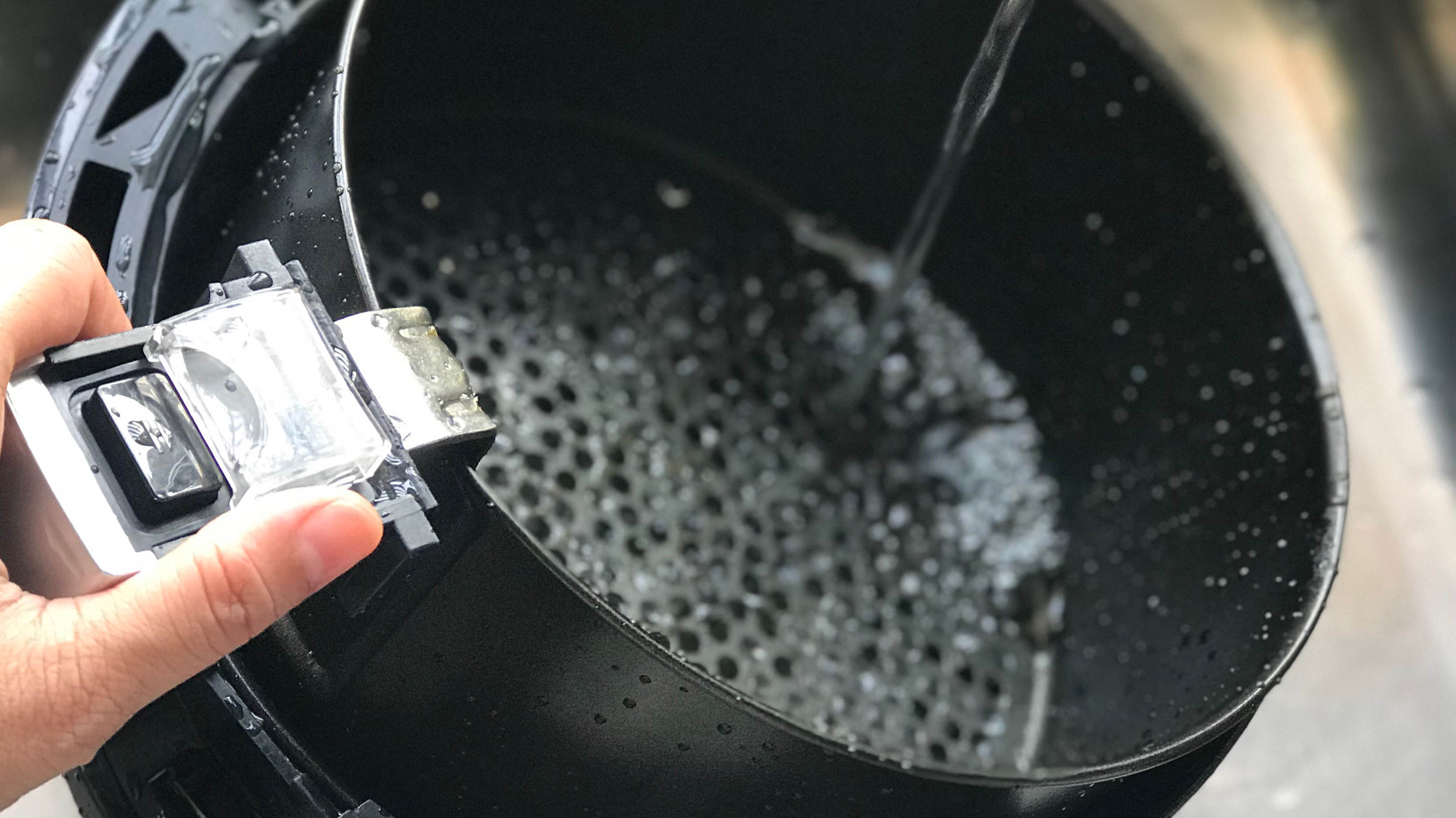 An air fryer basket being rinsed with water