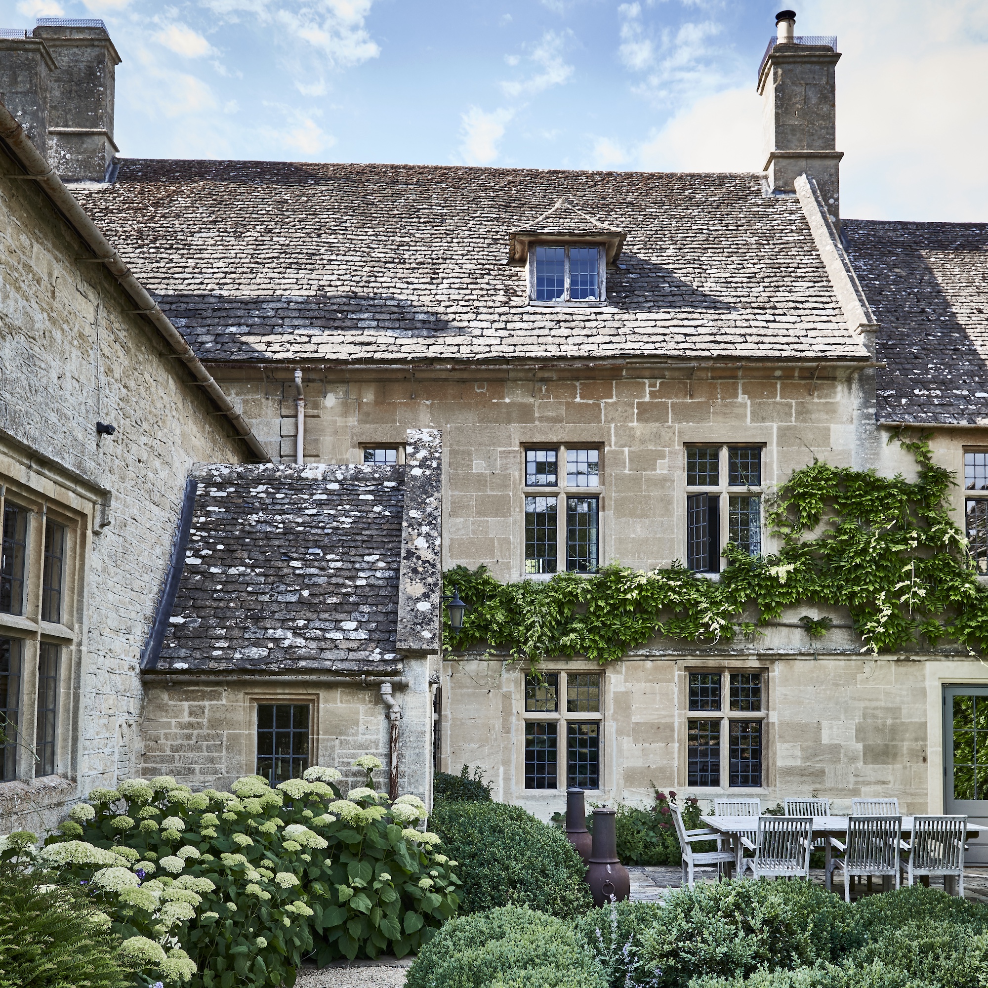 exterior of Cotswold stone manor house with hydrangeas and box shrubs in garden