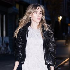 Suki Waterhouse wearing a black leather jacket, mini dress, and slouchy ankle boots