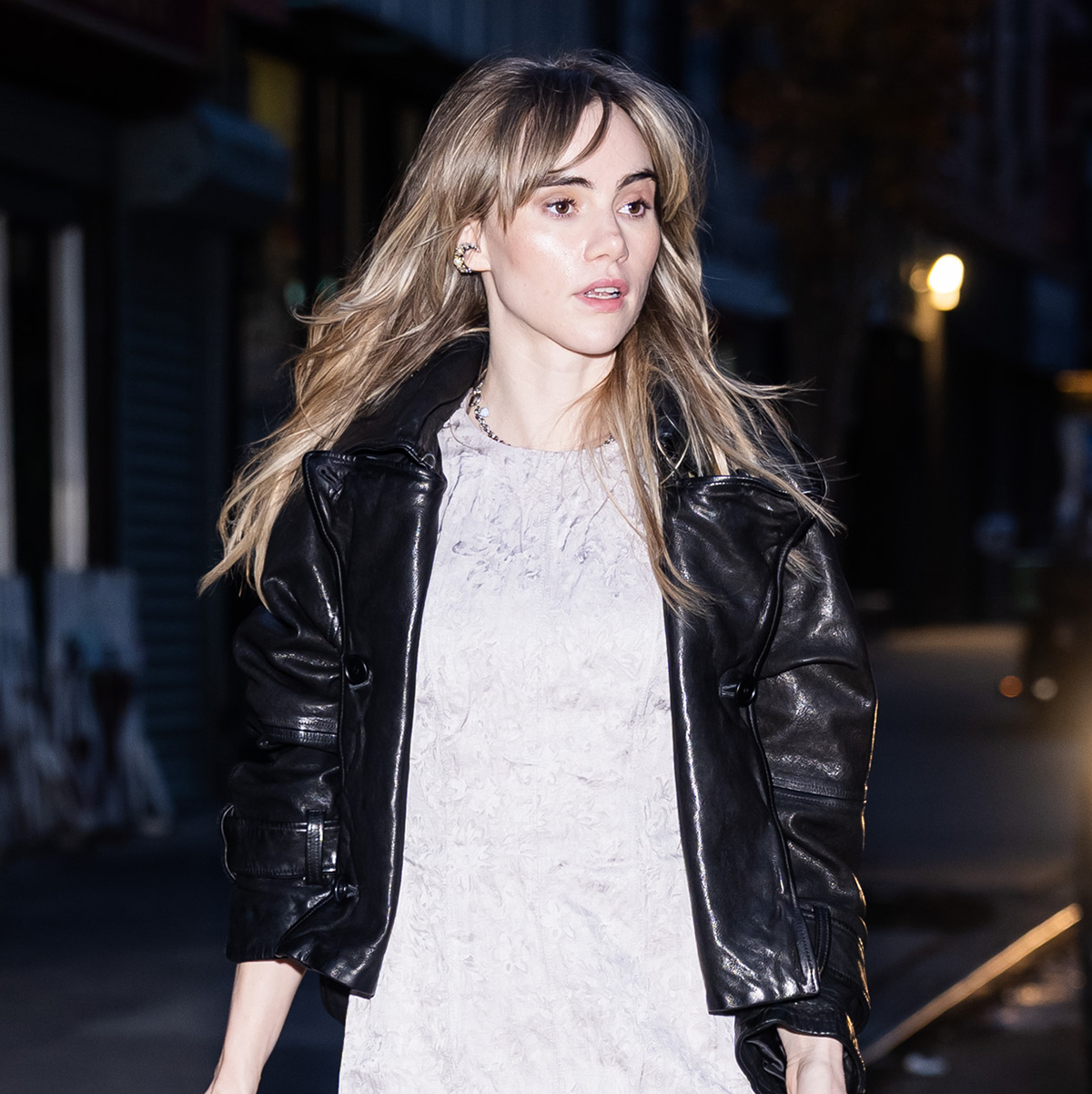 Suki Waterhouse wearing a black leather jacket, mini dress, and slouchy ankle boots
