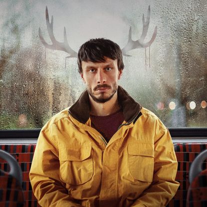 Richard Gadd as Donny Dunn, sitting at the back of the bus with reindeer antlers reflected in the window, in a promo image from the show 'baby reindeer'
