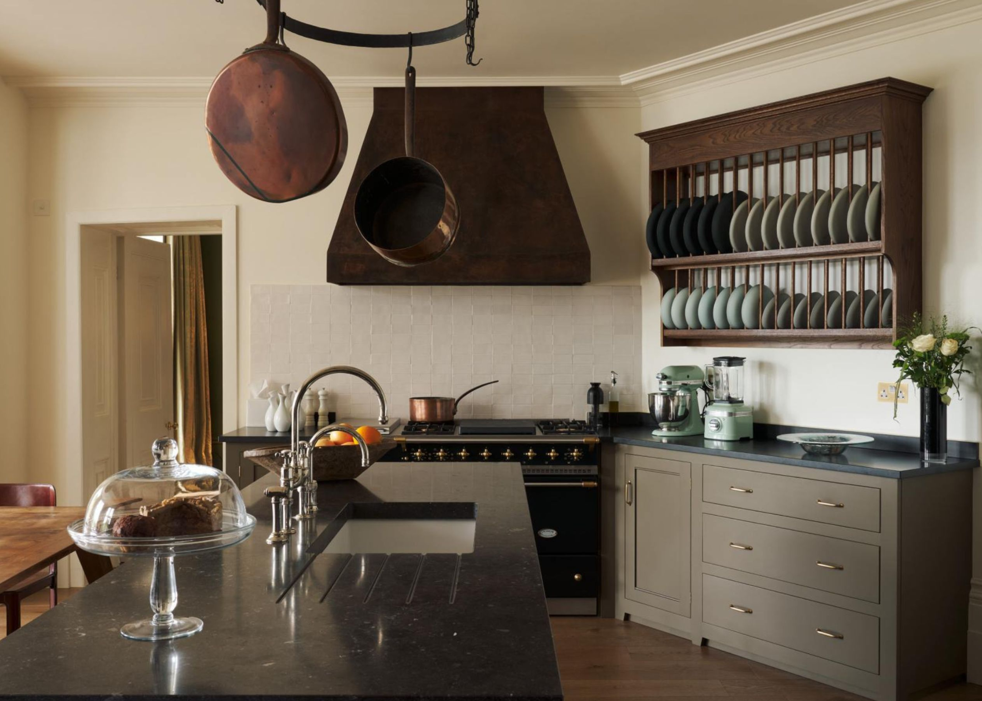 Open-plan farmhouse style kitchen with open shelving, copper pots and a granite work surface.