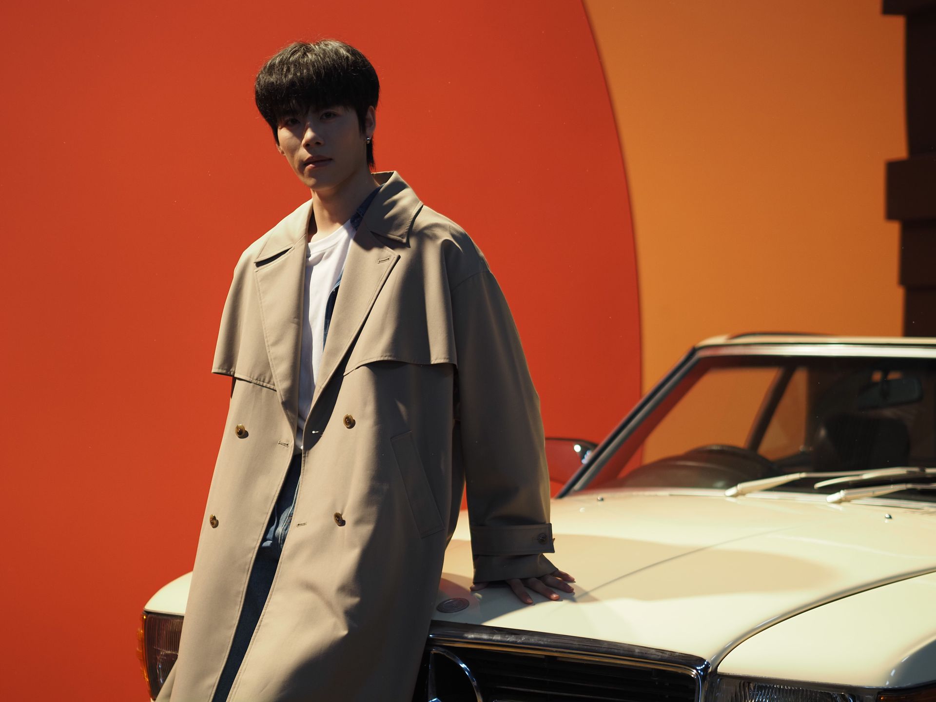  Male model in overcoat, leaning on a classic Mercedes car in beige, bright orange studio backdrop