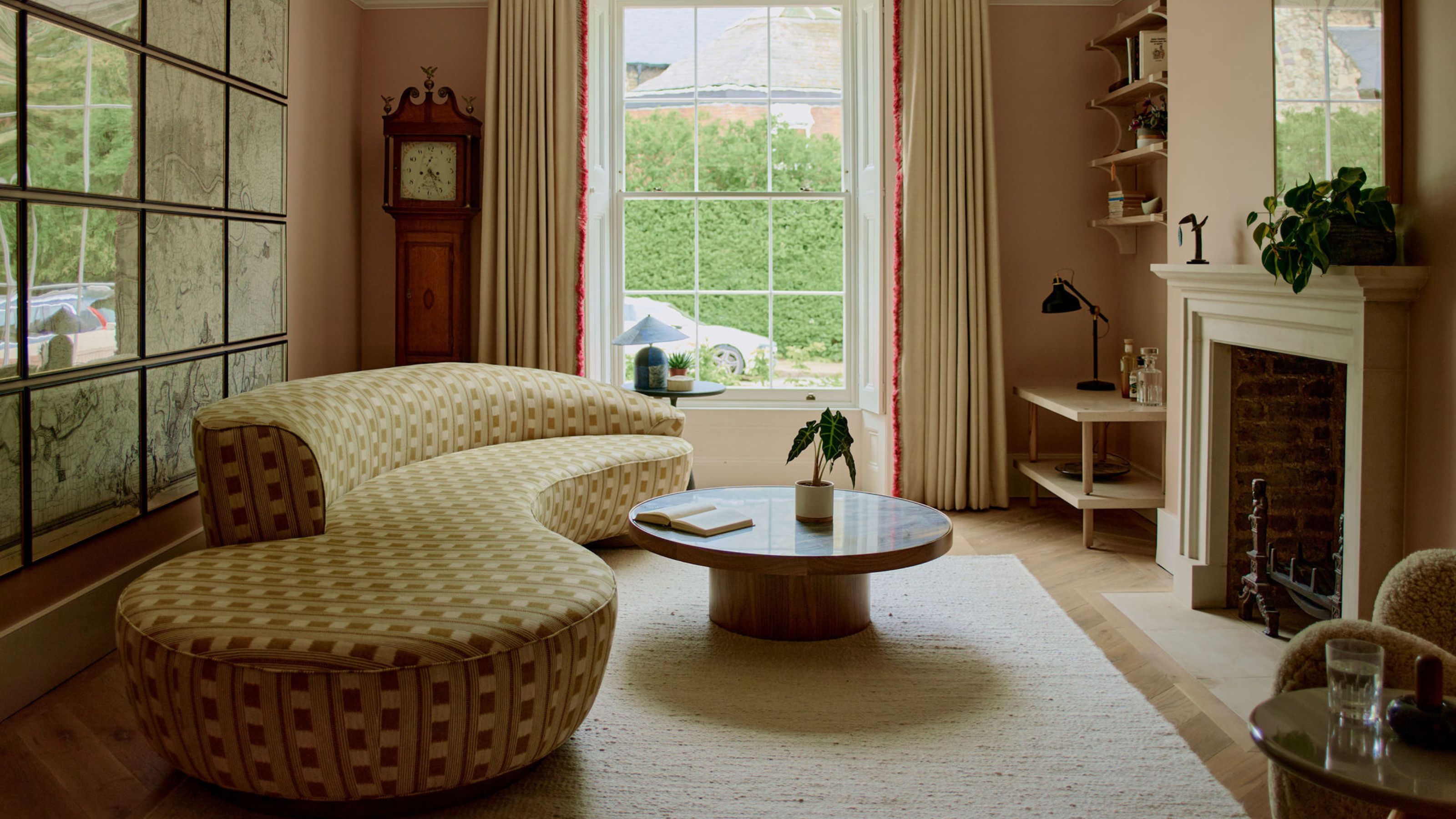 dusty pink living room with a traditional fireplace, a yellow checkerboard curved sofa, a gallery wall of art, and a circular coffee table