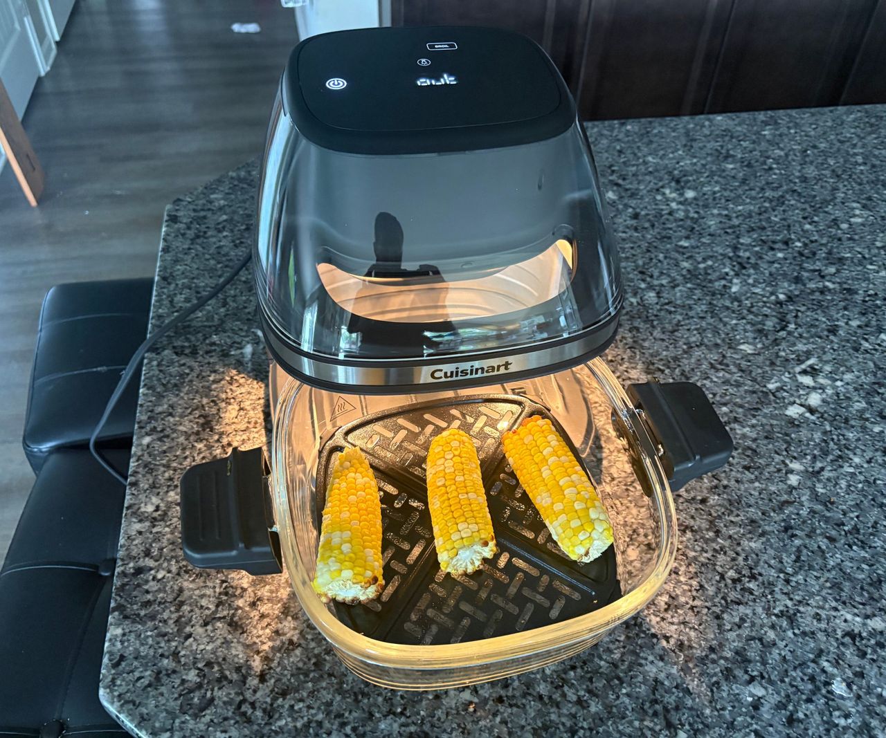 The Cuisinart glass air fryer on a granite countertop with three corn cobs inside.