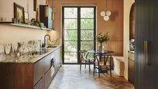 A kitchen with open shelving as well as a worktop and sink. There is also a section with a dining table and chairs as well as a vase and flowers on top of the table